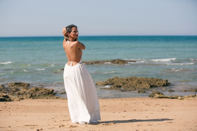 Vrouw in witte jurk en terug naar de lucht die op het strand staat