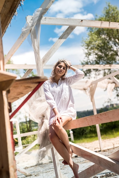 Vrouw in witte jurk geniet van een warme zomerdag in de buurt van het zandstrand in een wit houten prieel. vakantie of relaxen