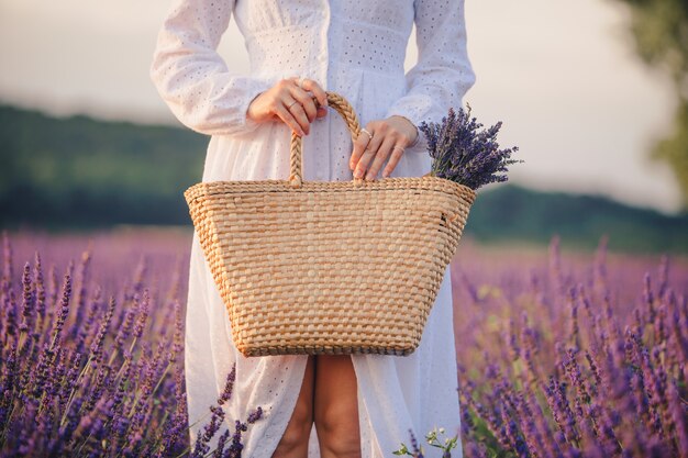 Vrouw in witte jurk met boeket lavendel bloemen in strozak close-up