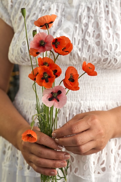 Vrouw in witte jurk met poppe bloemen, close-up op haar handen