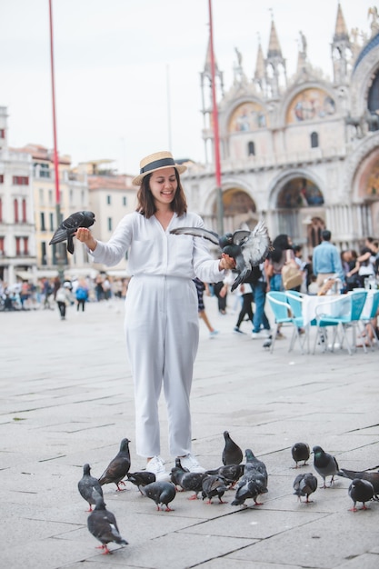 Vrouw in witte kleren met strohoed die plezier heeft met duiven op het plein piazza san marco . van venetië