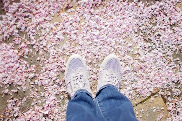 Vrouw in witte sportschoenen staat op de grond bedekt met sakura-bloemblaadjes zoals op een tapijt