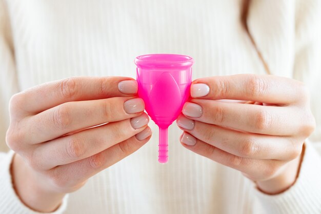 Vrouw in witte trui met roze menstruatiecup in handen close-up