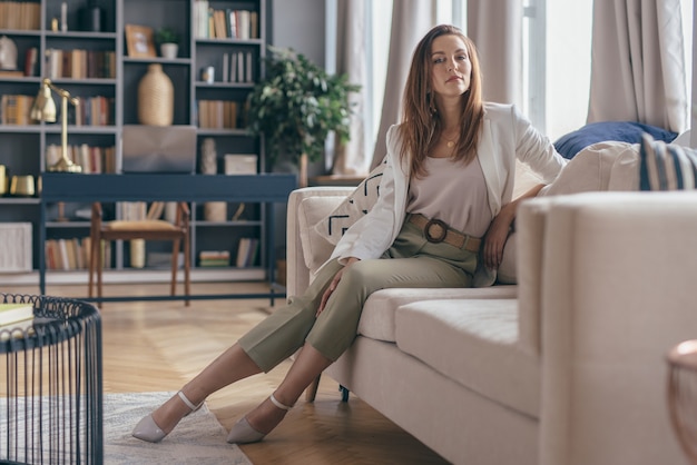 Vrouw in zakelijke kleding na het werk thuis rusten op de bank.