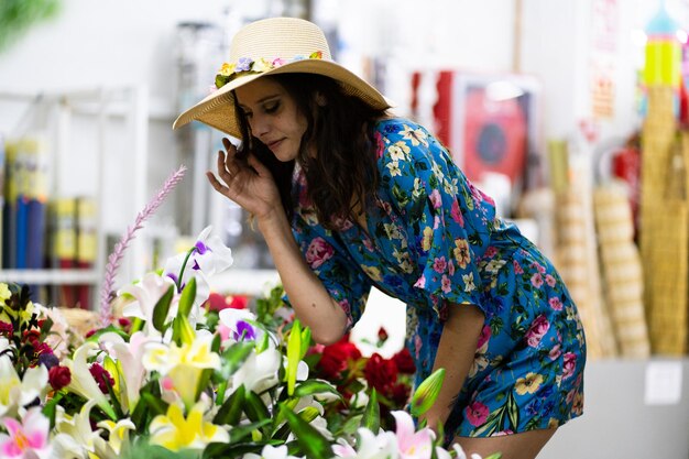 Vrouw in zomerjurk en strohoed die bloemen kiest uit een winkel