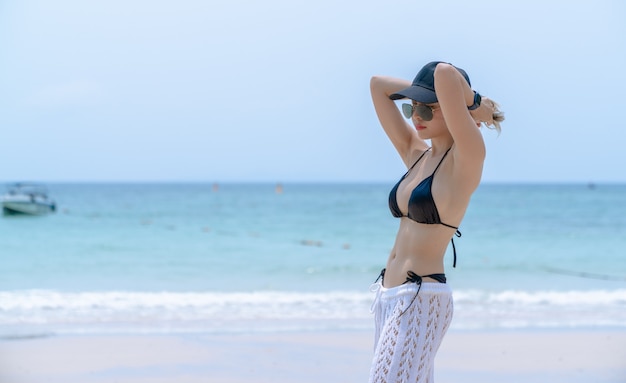 Vrouw in zwarte bikini op tropisch strand. Portret vrouw in badmode genieten en posten op het strand.