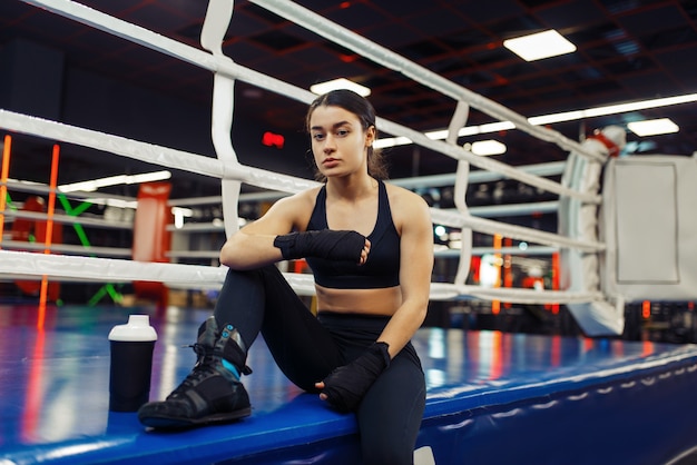 Vrouw in zwarte boksbandages zittend aan de touwen op de ring, vak opleiding. Vrouwelijke bokser in de sportschool, meisje kickbokser in sportclub, kickboksen training