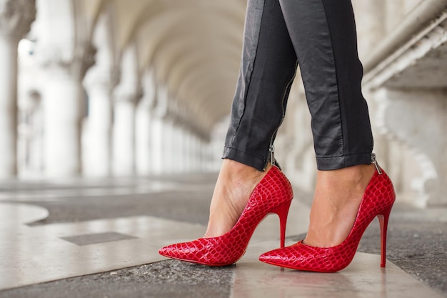 Vrouw in zwarte leren broek en rode schoenen met hoge hakken