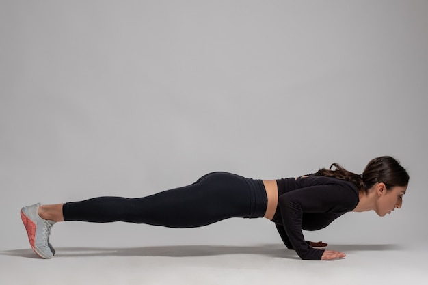 Vrouw in zwarte sportkleding die pushups doet op grijze muur