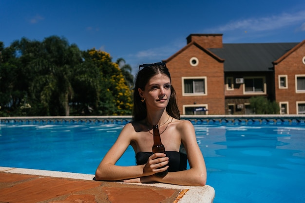 Vrouw in zwembroek drinkt een biertje in het zwembad.