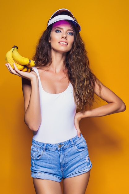 Vrouw in zwempak en blauwe borrels die banaan en stellen houden geïsoleerd over gele scène