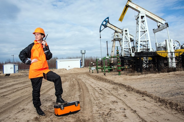 Vrouw ingenieur in het olieveld praten op de radio met oranje helm en werkkleding. Industriële site achtergrond.