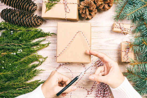 Vrouw inpakken kerstcadeau, meisje bereidt kerstcadeaus met dennenboom en dennenappel. Handgemaakt cadeau op houten achtergrond met kerstdecor. Bovenaanzicht, kopieer ruimte. afgezwakt.