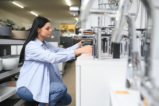 Vrouw inspecteert en kiest een nieuwe keuken- of badkraan in een ijzerwarenwinkel