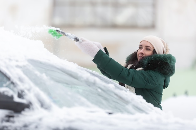 Vrouw is te klein om sneeuw van de bovenkant van haar auto te verwijderen nadat hevige sneeuwval voertuigen heeft achtergelaten die bedekt zijn met witte dekking.