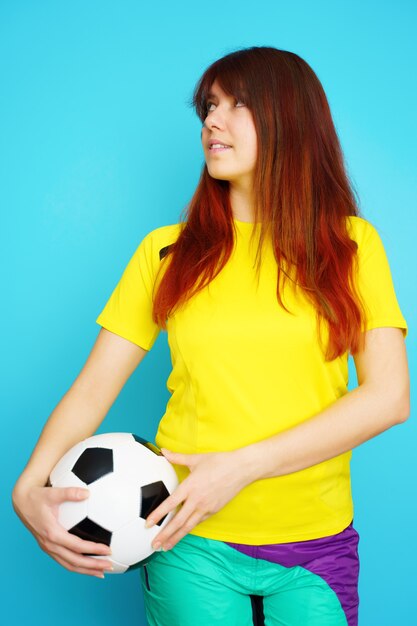 Vrouw is voetbalfan in geel t-shirt met voetbal op blauwe achtergrond