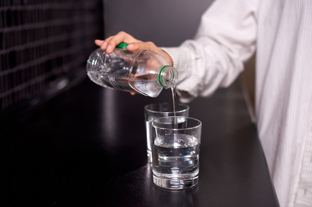 Vrouw is water uit plastic fles gieten in glas op zwarte tafel