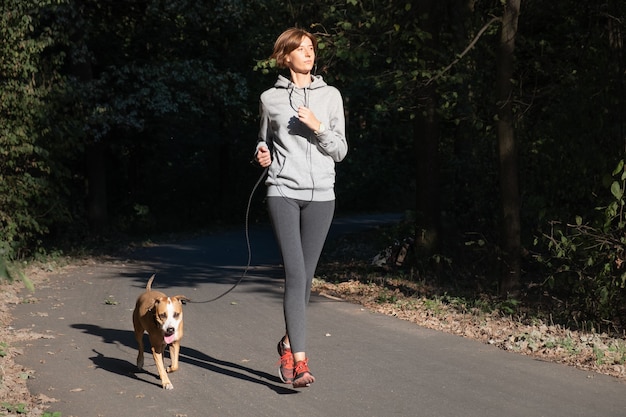 Vrouw joggen met hond in een park. Jonge vrouwelijke persoon met huisdier doet lopende oefening in het bos