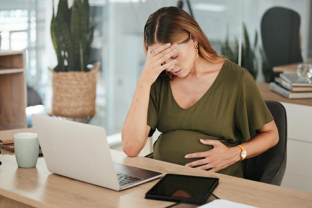 Vrouw kantoor en zwanger met stress hoofdpijn en laptop op het werk burn-out en werkplek Moederschap werknemer en zwangerschap met hand op buikpijn en moe voor baby werken en gezondheidszorg