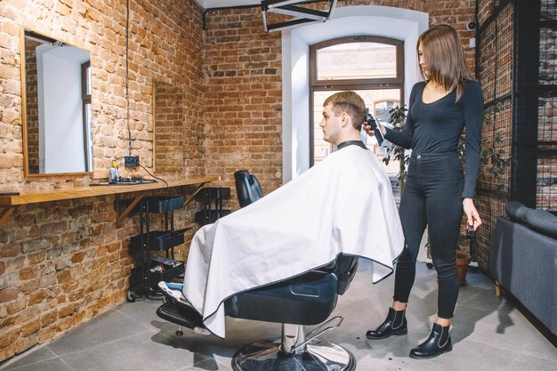 Foto vrouw kapper maakt een kapsel het hoofd van de klant met een elektrische trimmer in kapperszaak