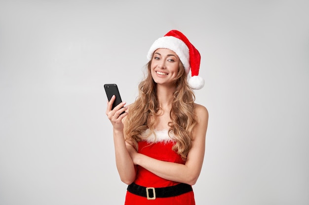 Vrouw kerst santa hat witte studio achtergrond met smartphone in de hand?