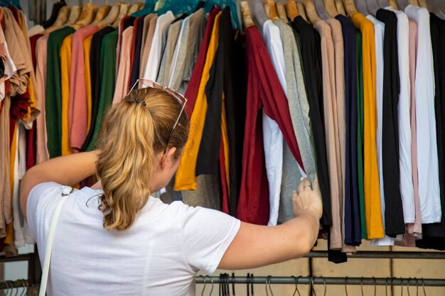 Foto vrouw kiest kleding die door de omroep in de winkel op de markt gaat. achteraanzicht