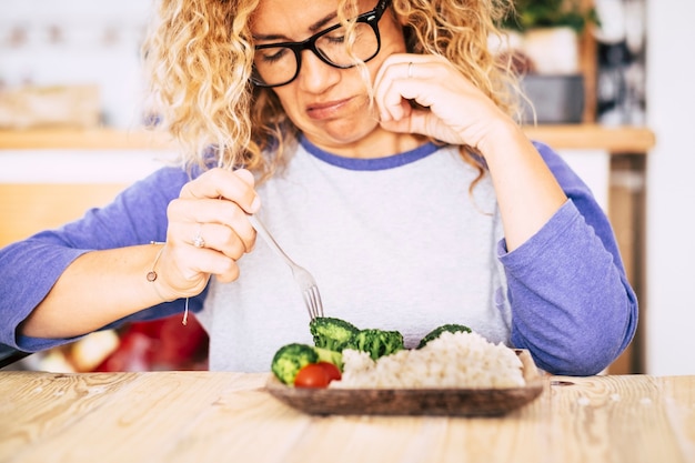 Vrouw kijkt met afschuw naar wat groenten en gaat op tafel staan - ze gaat dit niet eten omdat ze de voorkeur geeft aan slechte voeding - probeert af te vallen