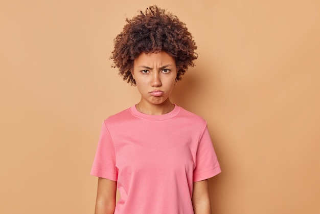 vrouw kijkt met mokkend fronsend gezicht wacht op uitleg of verontschuldiging geïrriteerd door oneerlijk ding draagt casual roze t-shirt geïsoleerd op beige voelt zich beledigd