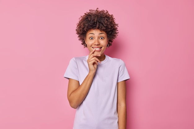 Vrouw kijkt met verrassing bijt lippen reageert op geweldig nieuws gekleed in casual t-shirt geïsoleerd op roze. mensen emoties en reacties concept