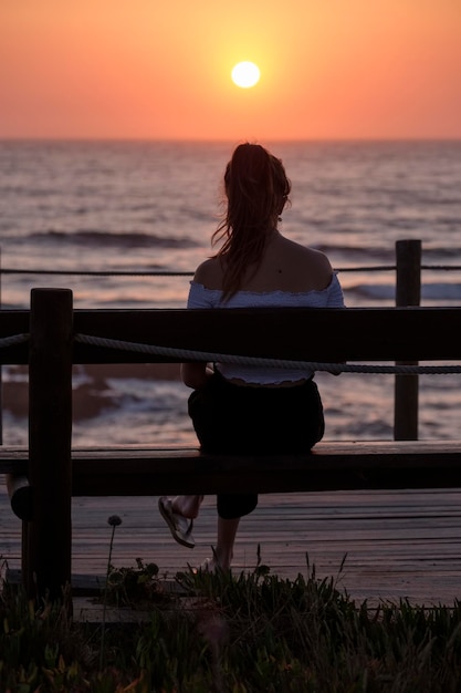 Foto vrouw kijkt naar de zee tegen de hemel bij zonsondergang