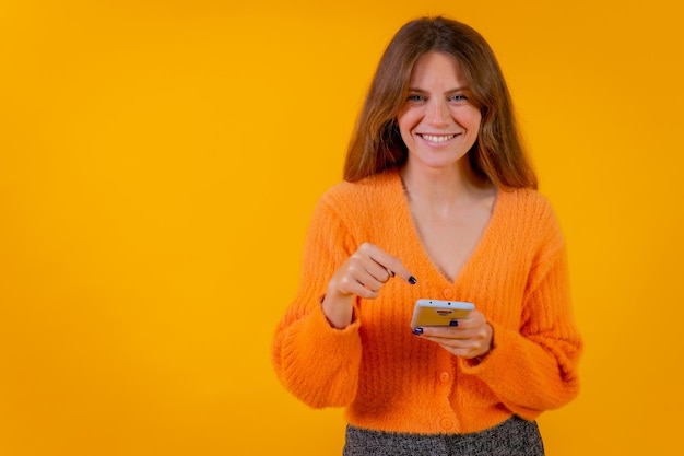Vrouw kijkt naar dingen op internet op de mobiele telefoon op een gele achtergrond online shopping concept