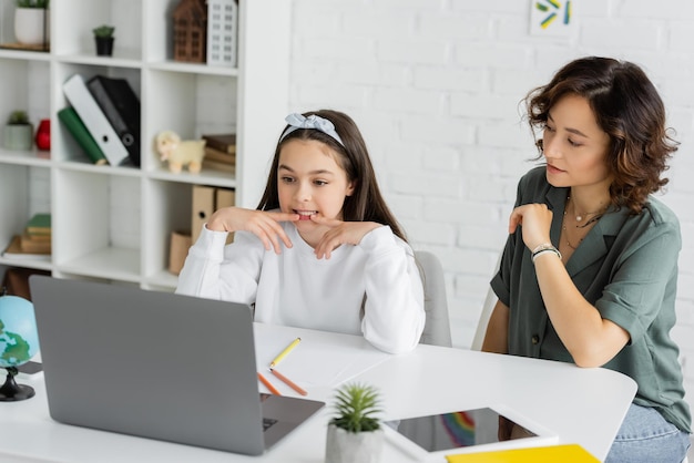 Vrouw kijkt naar dochter die praat tijdens een online les in spraaktherapie thuis