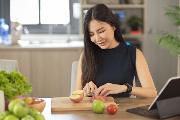 Vrouw kijkt naar het voedselrecept op een draagbare tablet terwijl ze de ingrediënten in haar keuken bereidt