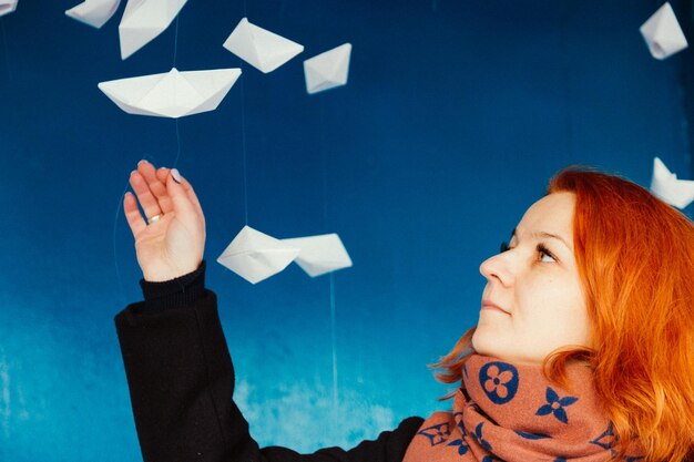 Vrouw kijkt naar papieren boten die aan de blauwe muur hangen.