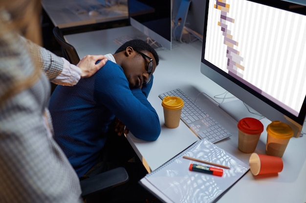 Vrouw kijkt naar slapende manager, nachtelijke kantoorlevensstijl. Vermoeide mannelijke personen op laptop, moderne werkplek