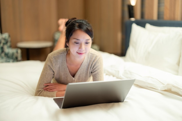 Vrouw kijkt op laptop en ligt thuis op bed.