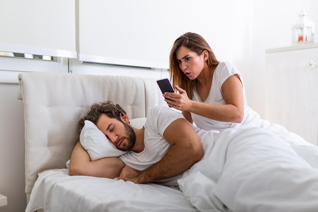 Vrouw kijkt stiekem naar de telefoon van de man terwijl de man slaapt. De vrouw bespioneert de telefoon van haar man terwijl hij slaapt. Het concept van wantrouwen, verraad, jaloezie, relaties, problemen.