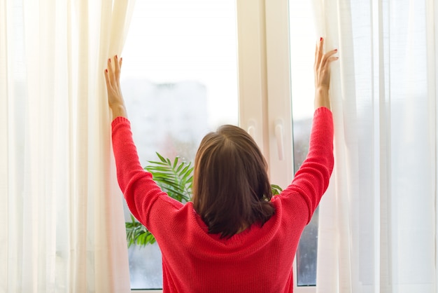 Vrouw kijkt uit het raam, opent de gordijnen