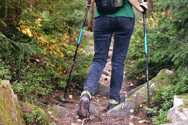 Vrouw klimt in wandelschoenen in buitenactie. Bovenaanzicht van Boot op het parcours. Close-up benen in jeans en sport trekkingschoenen op rotsachtige stenen van bergbos.