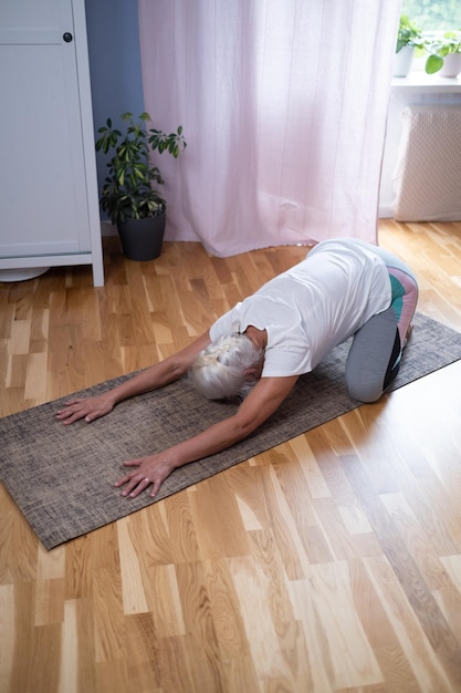 Foto vrouw knielt op een mat en doet een balasana-asana terwijl ze thuis yoga beoefent