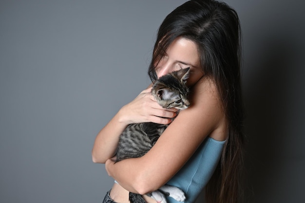 Vrouw knuffelen haar kitten Gestreepte kitten ligt op de schouder van een vrouw op een grijze achtergrond