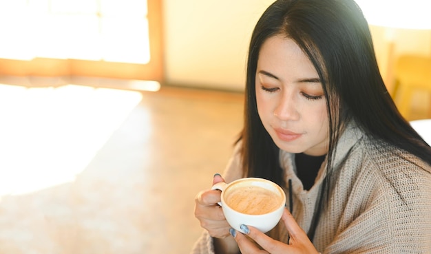 Vrouw koffie met de hand met een kopje in cafe jonge vrouw koffie drinken ontspannen vrouw ruikende koffie thuis in de winter met kopje koffie