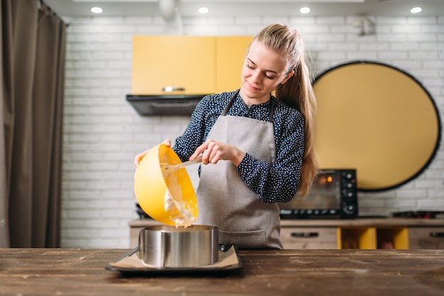 Vrouw kok in schort voegt room voor de cake toe aan de pan.