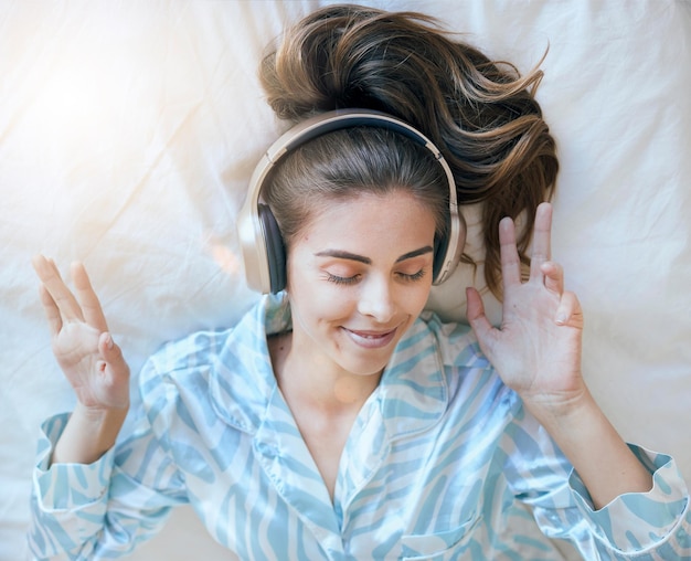 Vrouw koptelefoon en muziek luisteren in bed om thuis te ontspannen podcast of radio streaming vrede en tevredenheid Jonge wellness en positiviteit in slaapkamer mentaliteit en zelfzorg luister en vrijheid