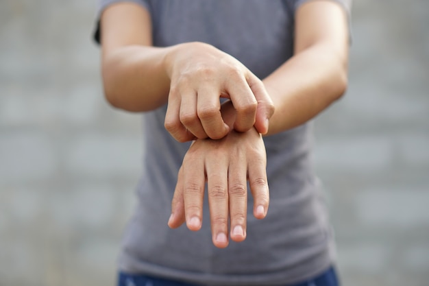 Vrouw krabt arm van jeuk op lichtgrijze achtergrond Oorzaak van jeukende huid is onder meer insectenbeten