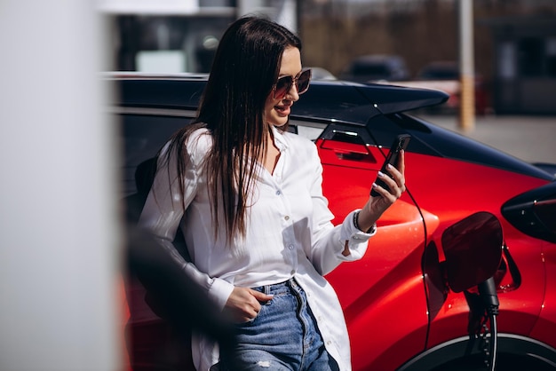 Vrouw laadt elektrische auto op en praat aan de telefoon