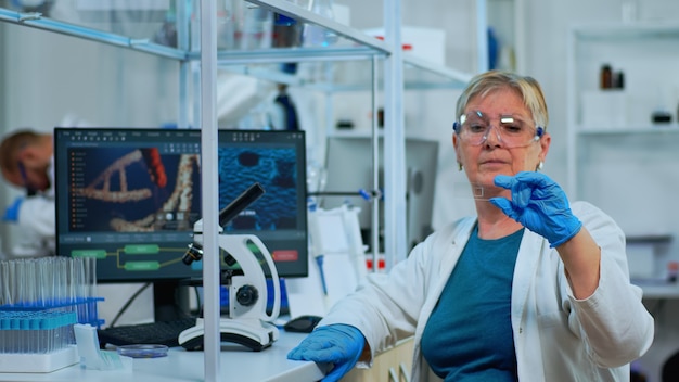 Vrouw laboratoriumtechnicus kijken naar virusmonster in modern uitgerust laboratorium. Senior wetenschapper die werkt met verschillende bacterieweefsel- en bloedonderzoeken, concept van farmaceutisch onderzoek voor antibiotica