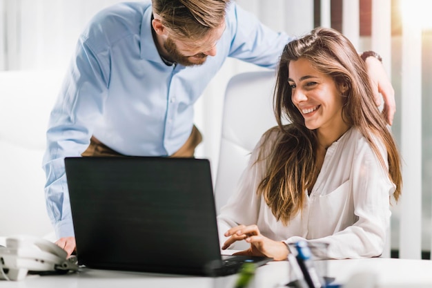 Vrouw lacht met collega terwijl ze laptop op het bureau gebruikt