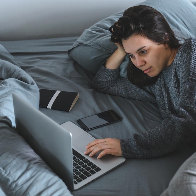 Vrouw lag in bed met grijze lakens. film kijken op laptop in bed. levensstijl concept