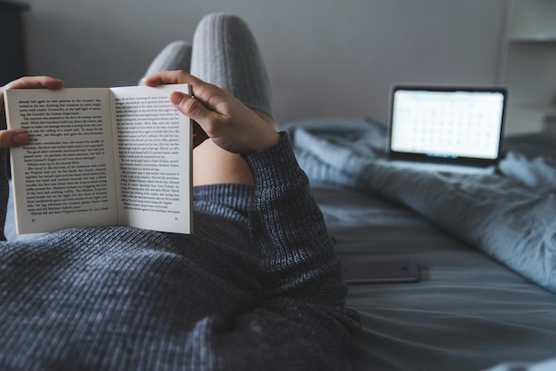 Vrouw las boek in bed. laptop op de achtergrond. studeren in bed